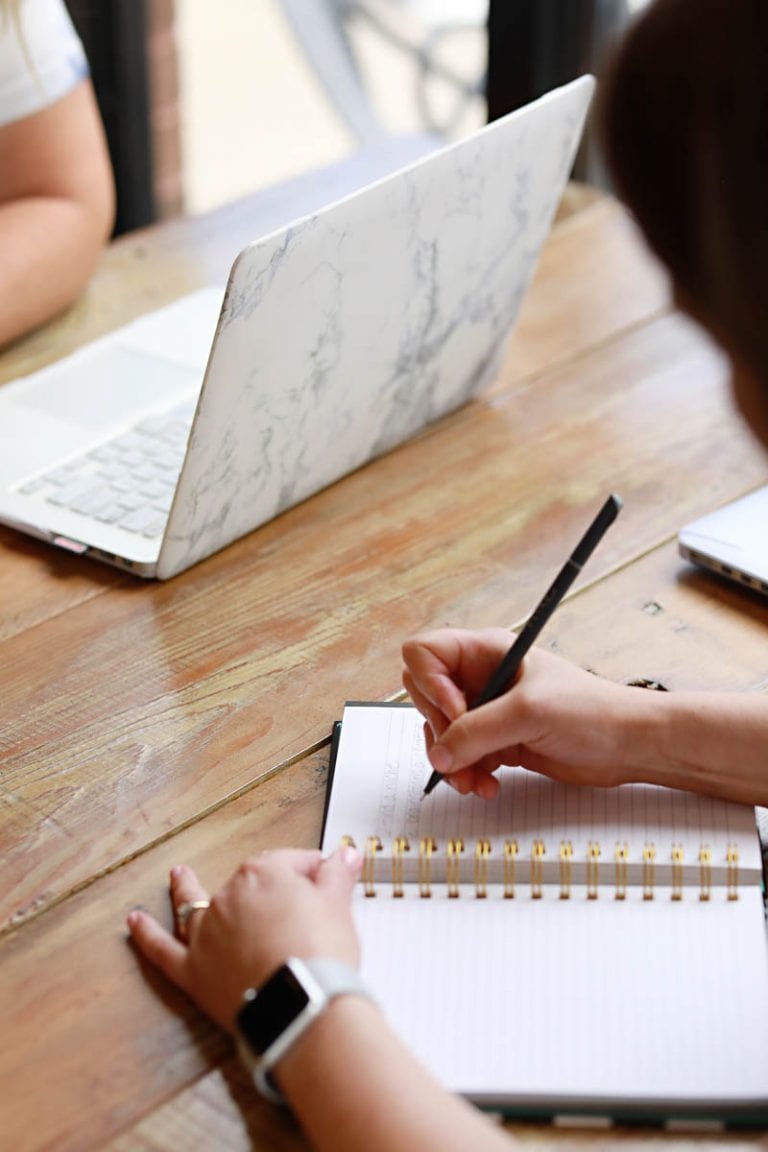a woman writing in a journal and another person on a computer