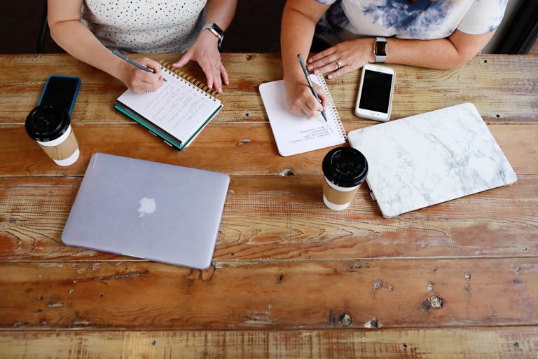 two women sitting at table writing notes