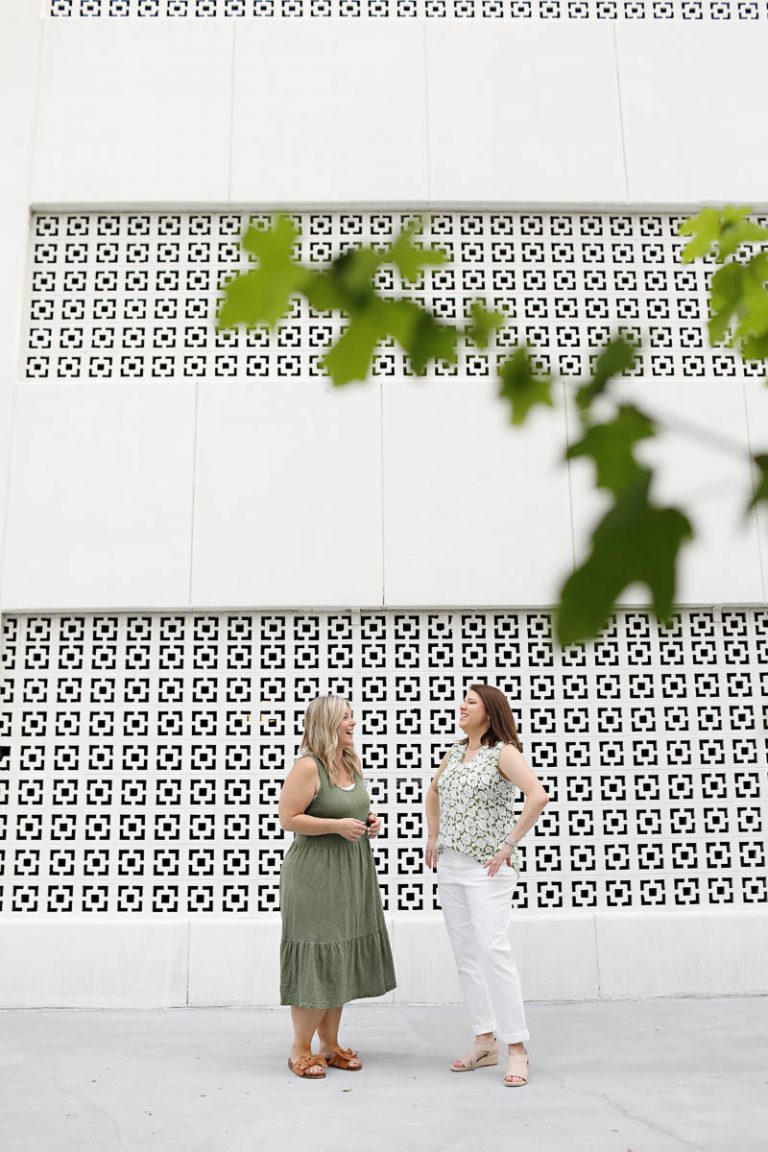 two women standing in front of a white building talking