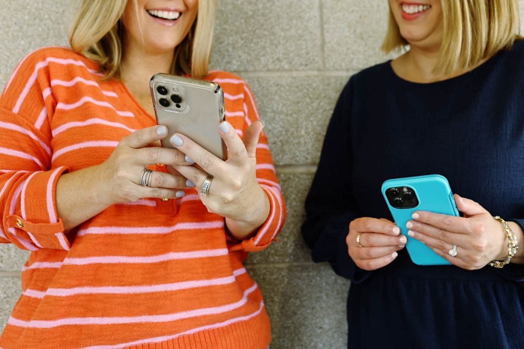 two women looking at their phones and smiling