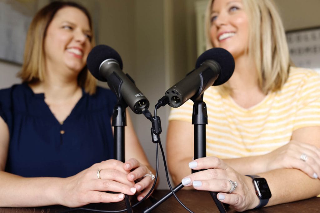 two podcasting microphones with women in background