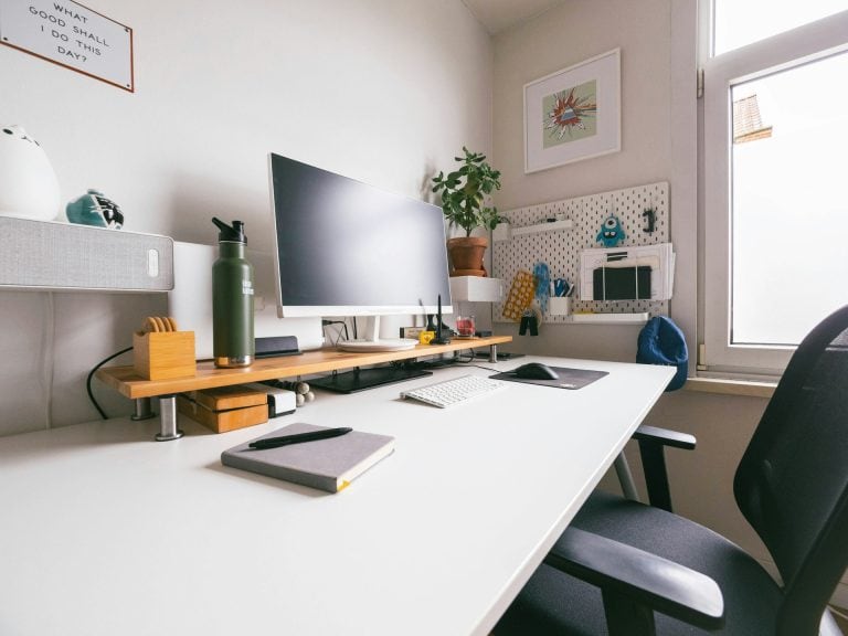 Desk next to a window with desktop computer and office supplies